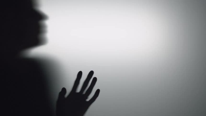 A silhouetted woman stands behind a sheet