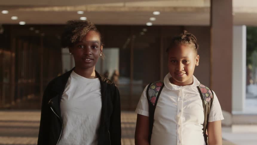 Two girls stand outside of a school building