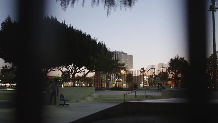 Skateboarders ride in a city skate park at dusk