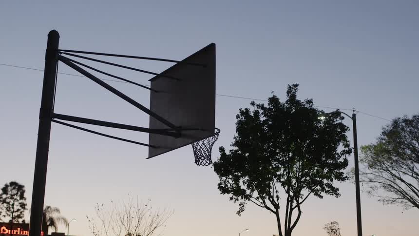 A basketball hoop sits on an outdoor court at dusk