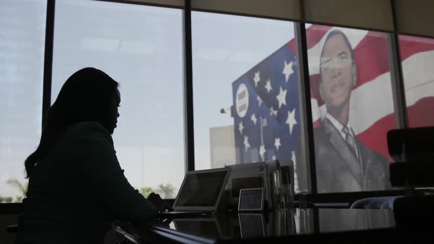 A woman sits at a desk with a large mural visible through the window