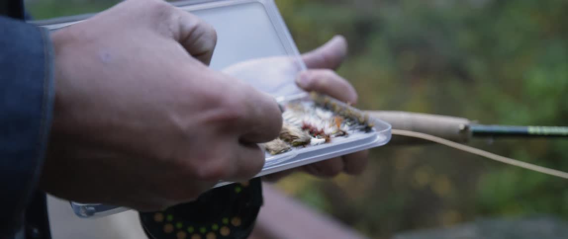 A man is picking out a lure from a box as he fishes during the day
