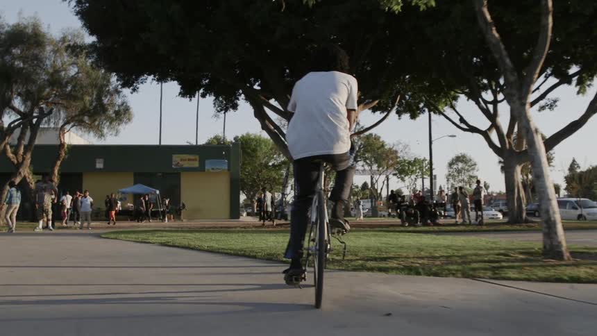 Man rides a bike towards a building with many people outside of it