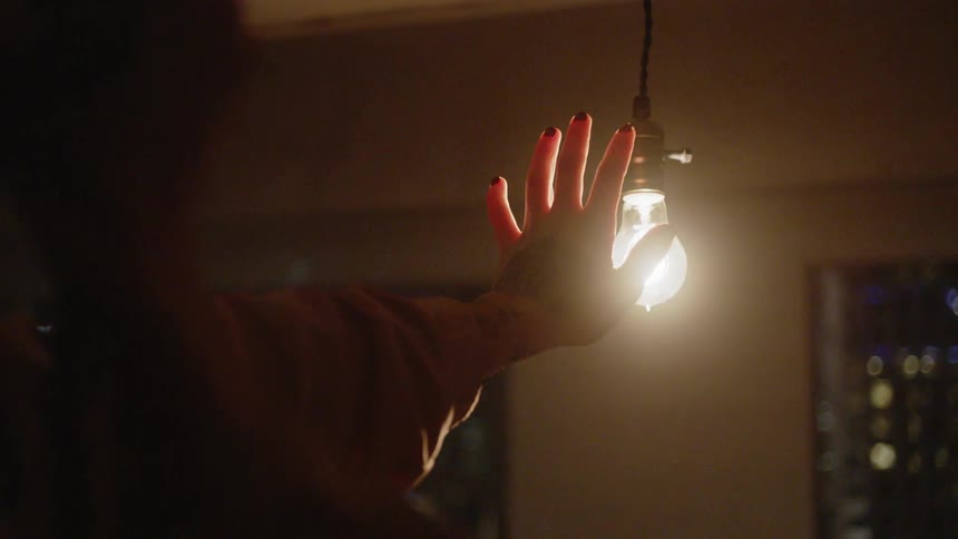 A woman holds her hand in front of a glowing light bulb