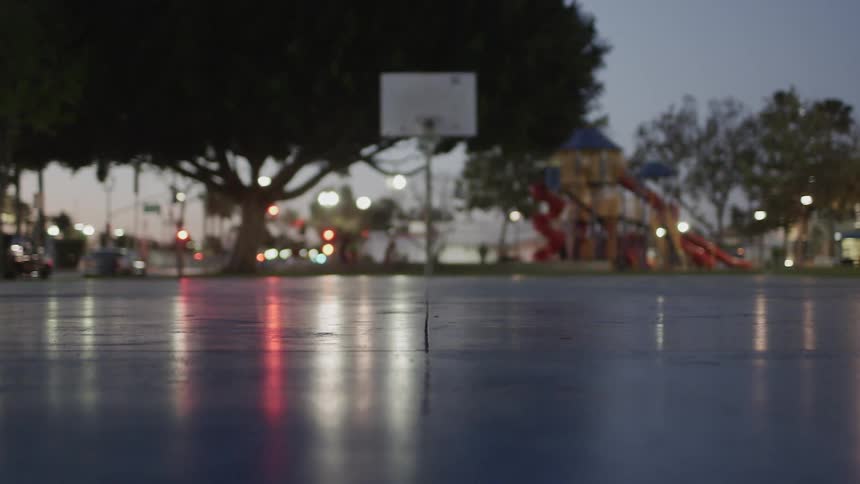 A basketball hoop sits in the middle of an outdoor court on a rainy night