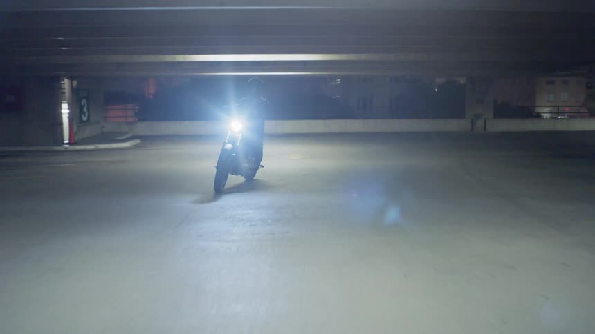 A woman rides a motorcycle in a parking garage