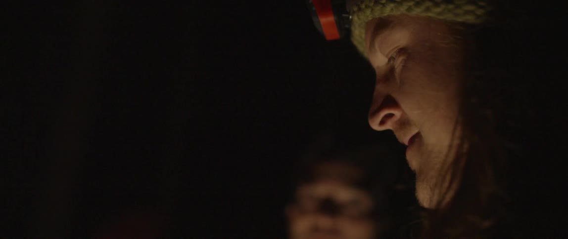 Men sitting at a campsite laugh and talk at night