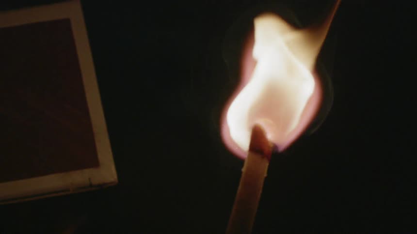 A match burns in a dim room