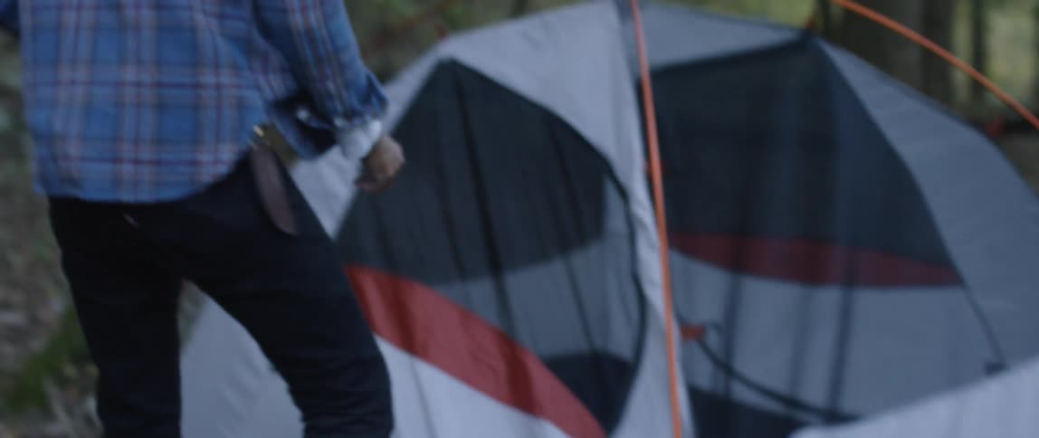 A man is taking down his tent outside during the day