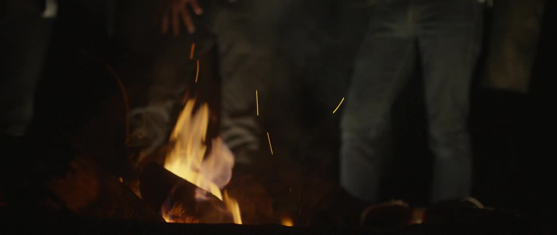 People stand next to a campfire at night