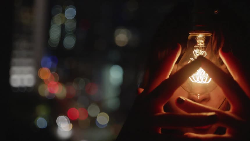 A woman holds her hands near a glowing light bulb