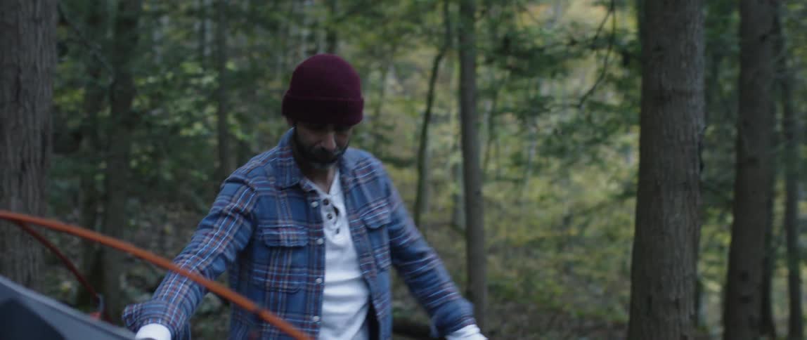 A man is dismantling his tent outside in a wooded area in daylight