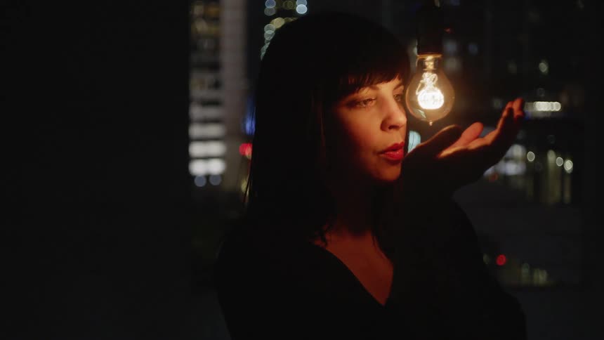 A woman examines a light bulb at night
