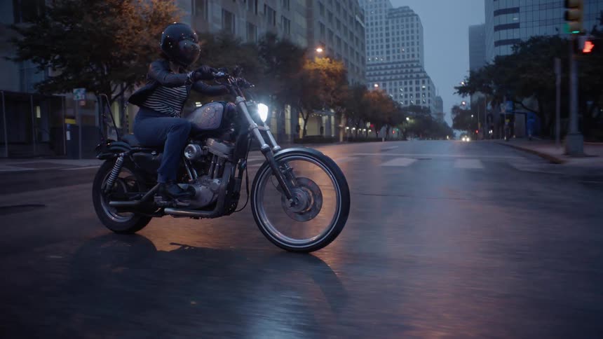 A woman rides a motorcycle down a city road