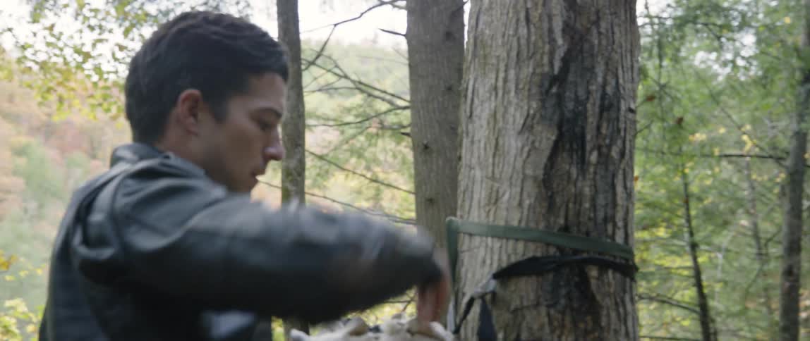 A man ties a bag to a tree in the woods