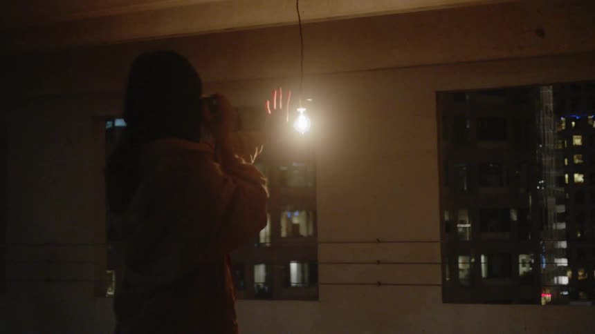 A woman photographs her hand in front of a glowing light bulb