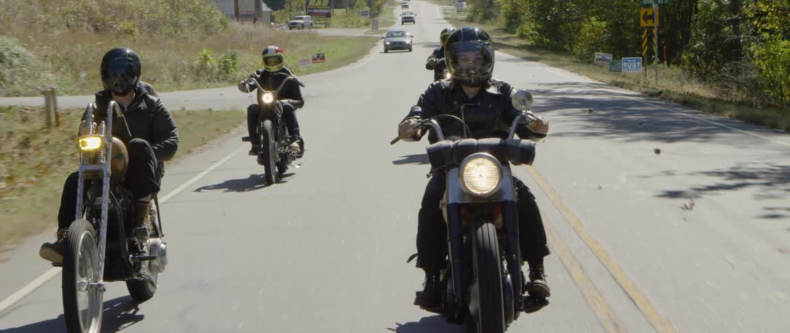 A group of motorcyclists are riding on a rural road during the day