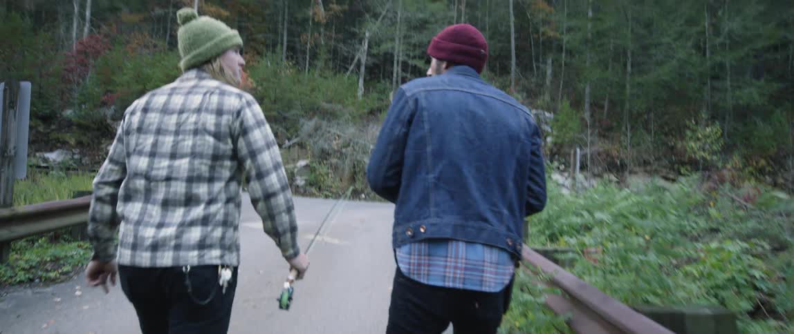 Two men walk with fishing poles in a forest