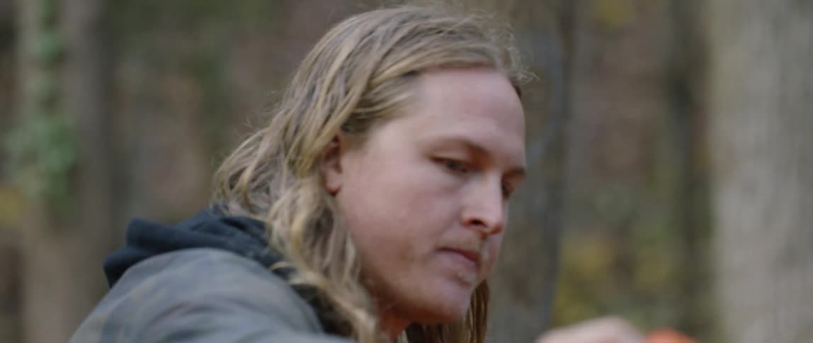 Man walks outside in the woods straightening a piece of cloth