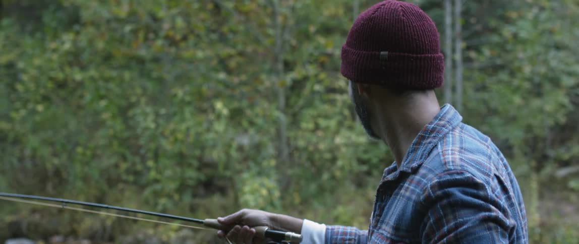 Man wearing a toque fly fishing in a creek