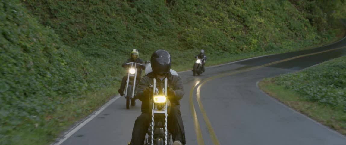 Four people ride on motorcycles on a country road through the mountains