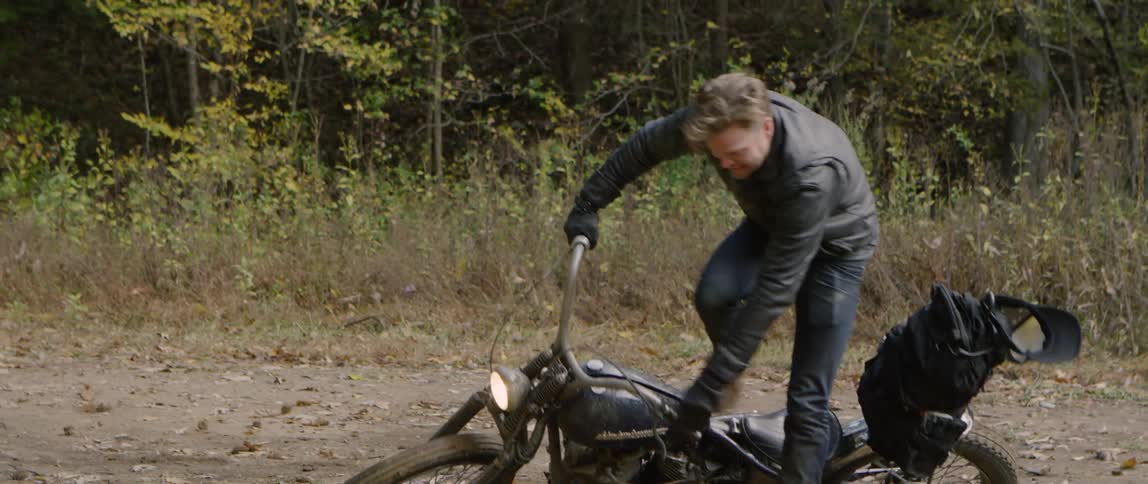 A man spins out and drops his motorcycle while riding on a dirt road in daylight