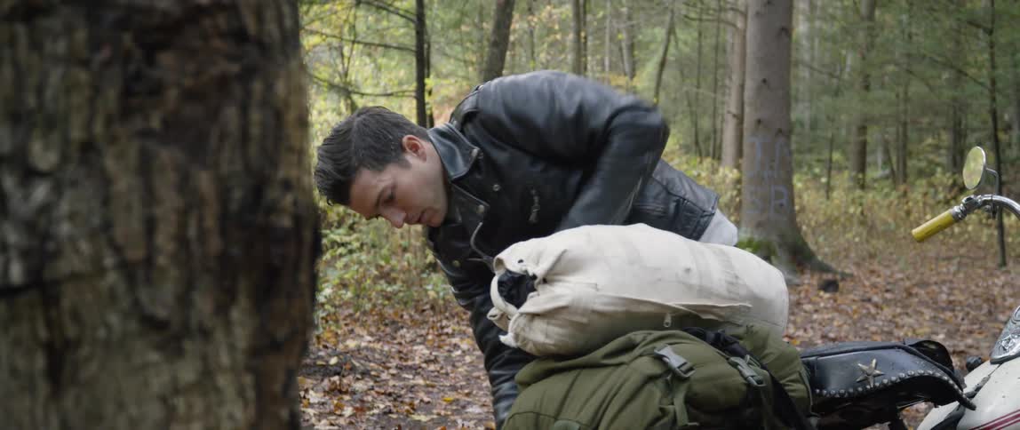Man unfastens duffel bag from motorcycle in the woods