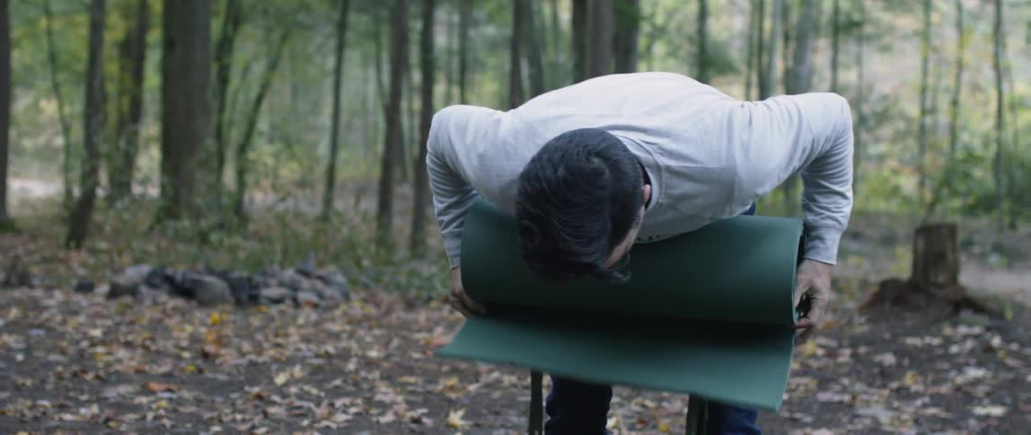 A man rolls up a sleeping pad in the woods
