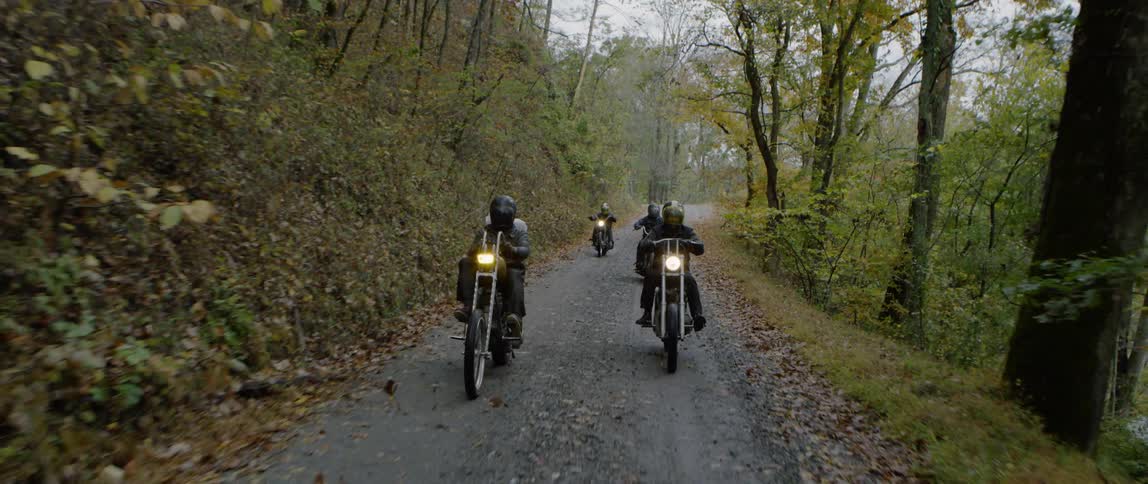 People ride motorcycles on a dirt road in the woods