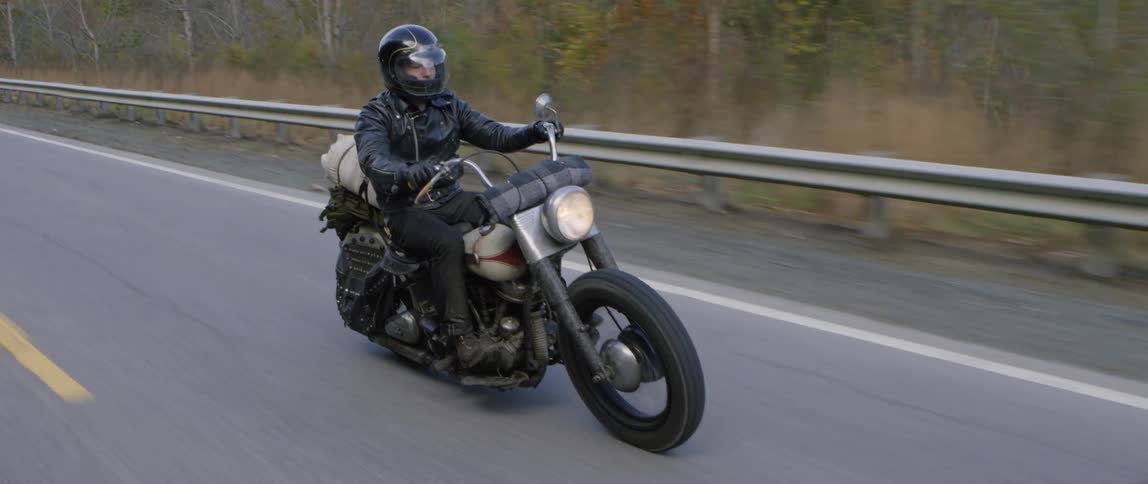 A man rides a motorcycle down a two lane road