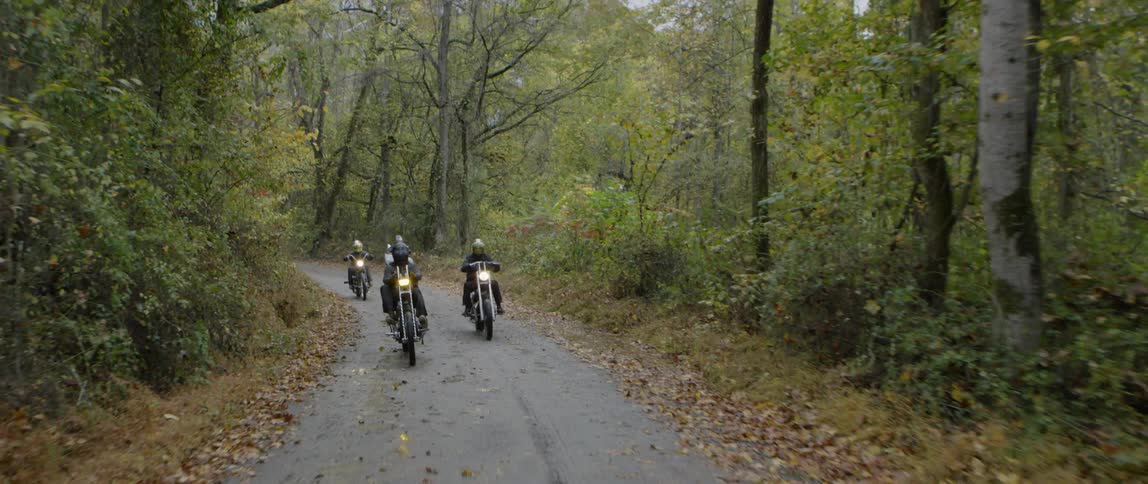 Motorcyclists riding a small road through a forest on a fall day
