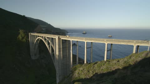A bridge gaps two cliffs with boats in the water below