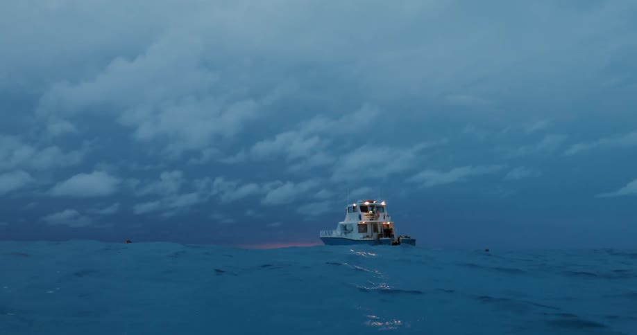 A diver is floating at the surface of the ocean near a boat at dusk