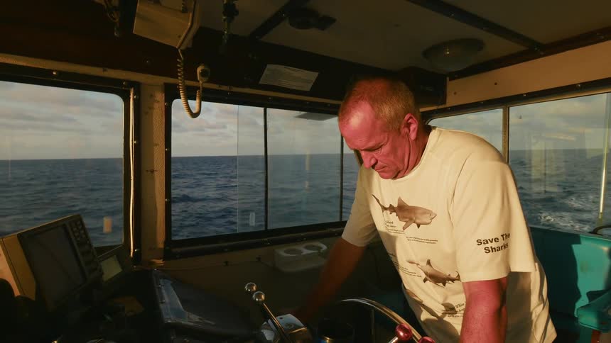 A man is steering a boat as it sails during the day