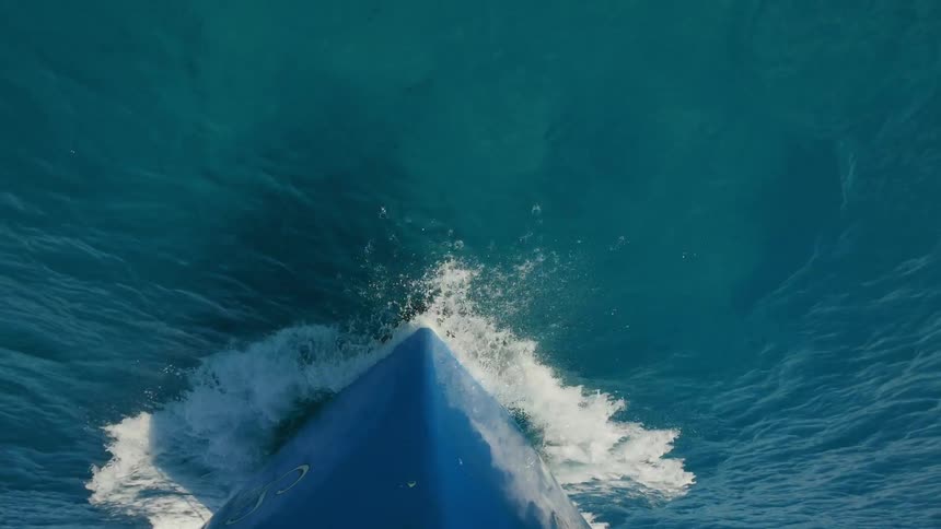 The bow of a boat is breaking through the water as it sails during the day