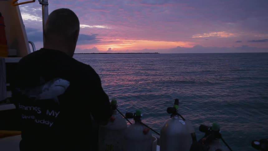 A man takes a photograph of the sunset over the ocean from a boat