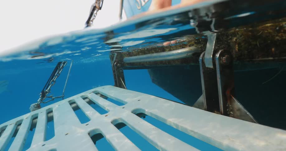 A person dangles their feet in the water off a boat