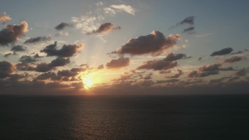 The sun is setting beyond billowing clouds over the ocean