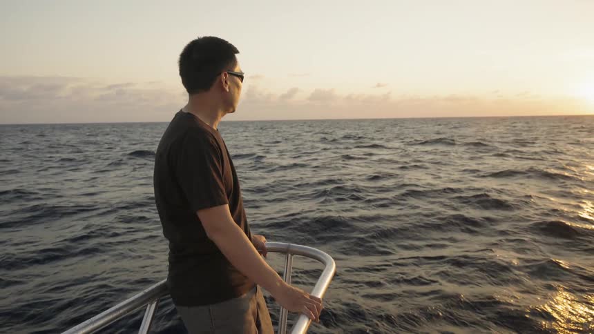 A man rides on the front of a boat at sunset