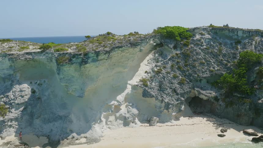Person walks on the edge of a cliff near the ocean on a sunny day