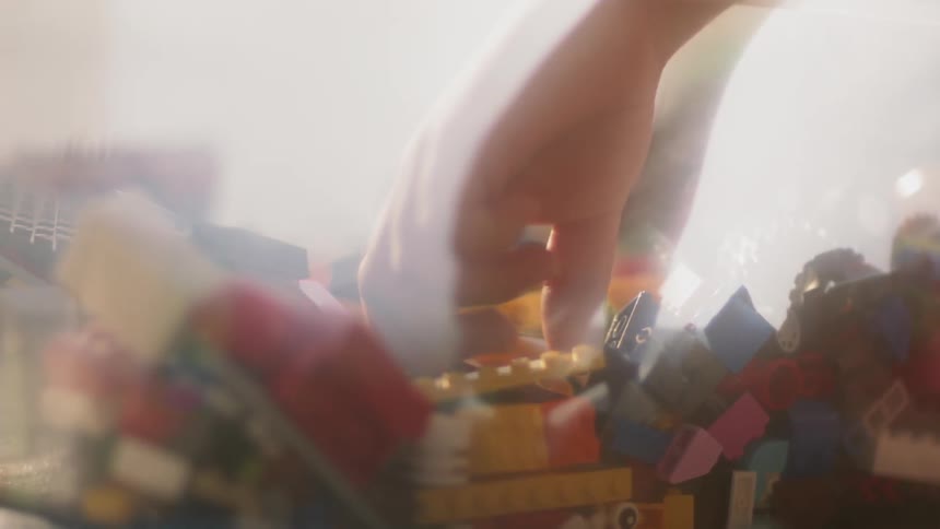 A child's hand drops then picks up a small toy block