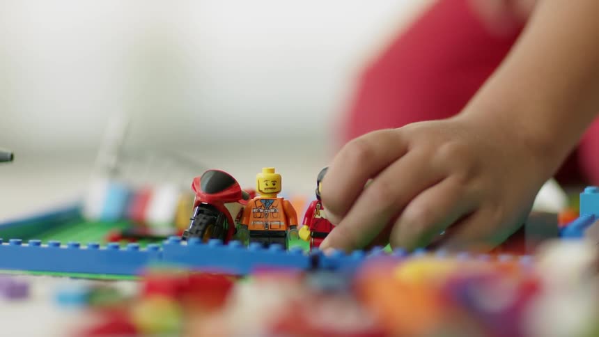 A child is playing with building block characters and bricks on the ground in a room in daylight