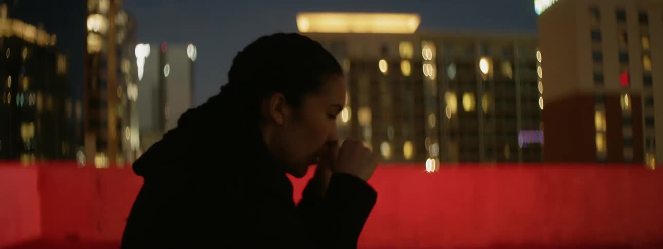 A woman punches the air on a city rooftop at night