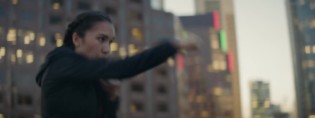 A woman is shadow boxing on a rooftop at sunset