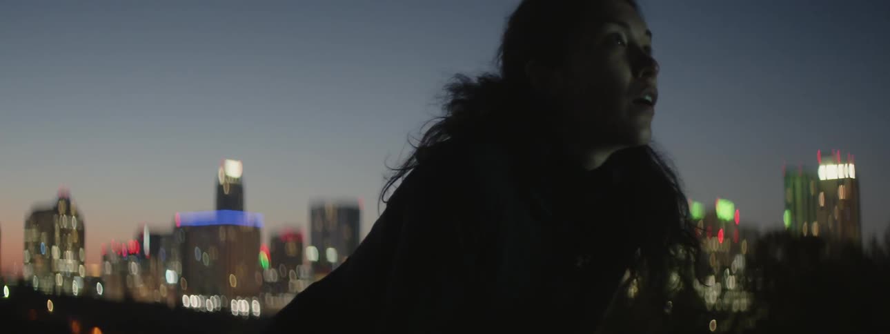 A female athlete is breathing heavy as she rests on a city rooftop at dusk