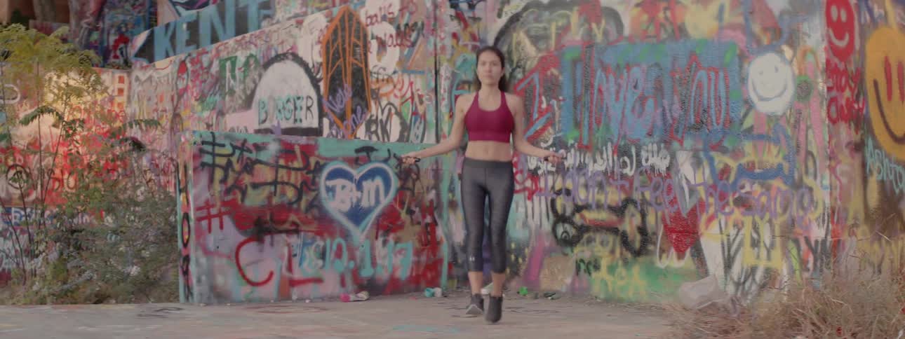 Woman jumping rope in a city next to a wall with heavy graffiti