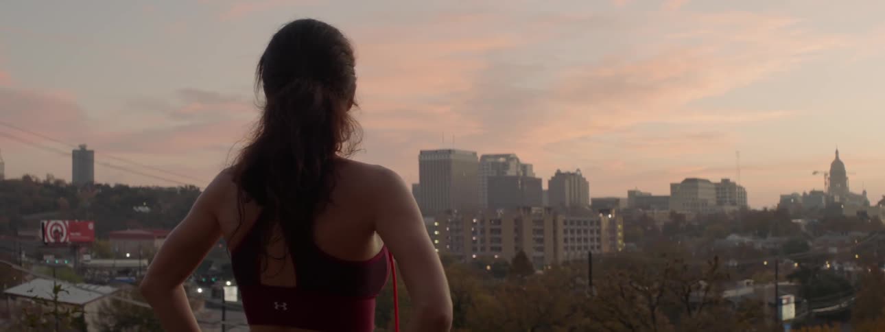 A woman stands on a rooftop looking out onto a city