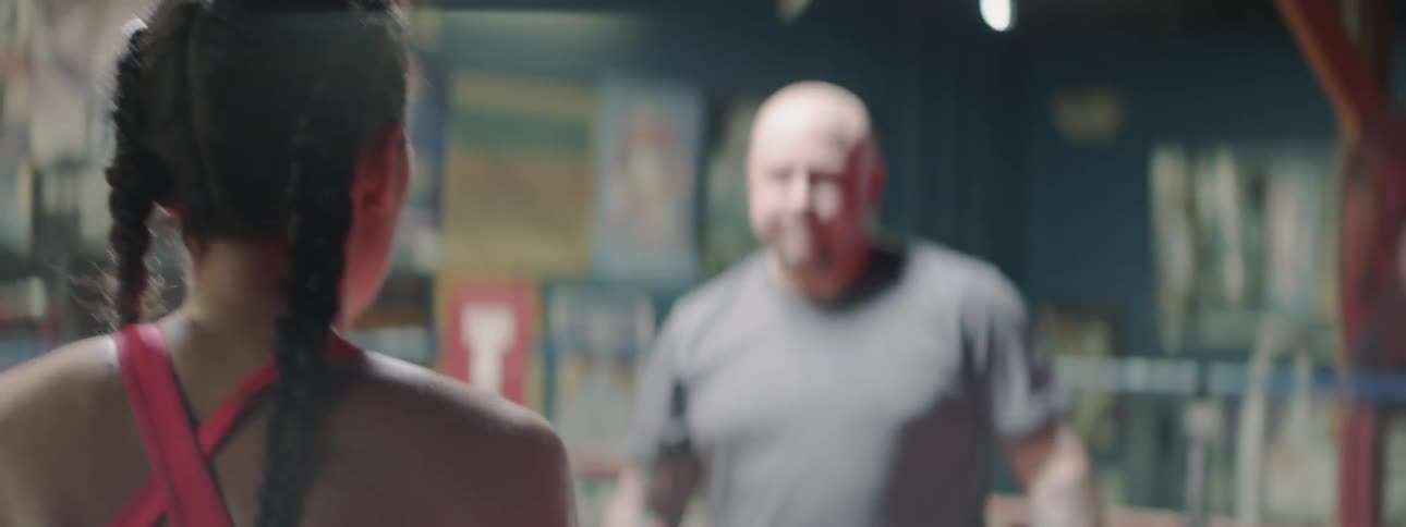 A female boxer is training with a coach in a boxing ring in a gym