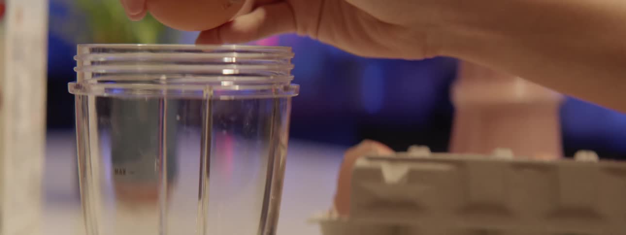 A woman is putting a raw egg into a blender cup