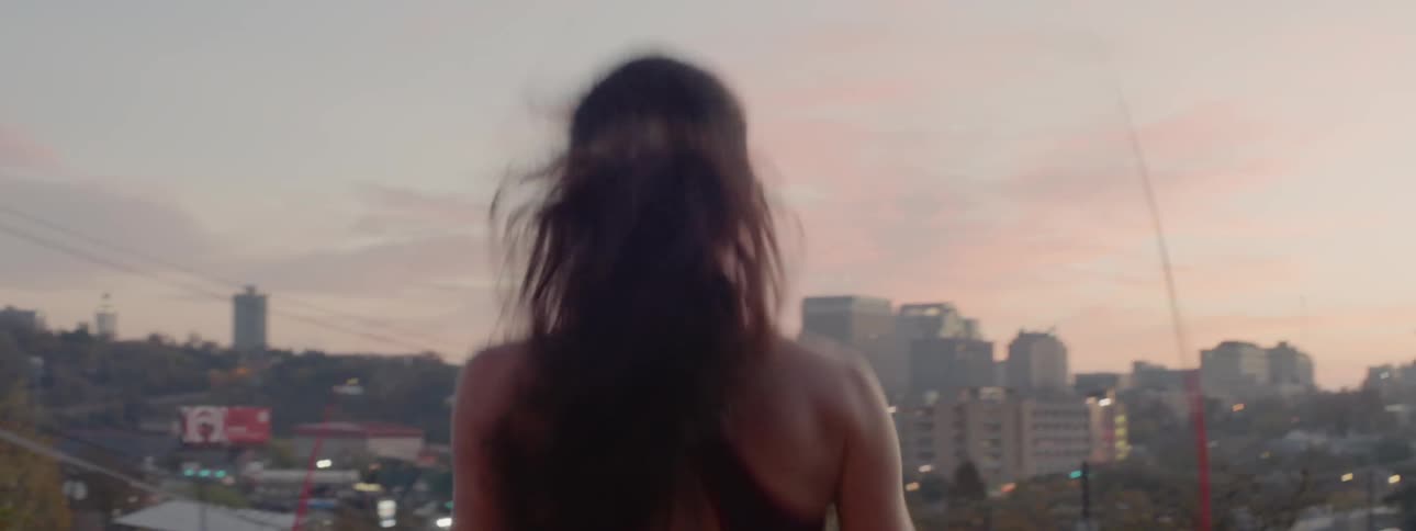 A woman jumps rope while overlooking a city at sunset